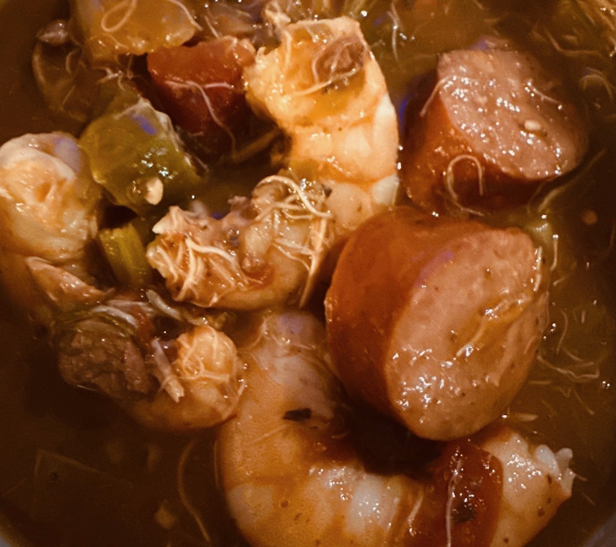 Close-up of shrimp, sliced sausage, and vegetables in a rich broth