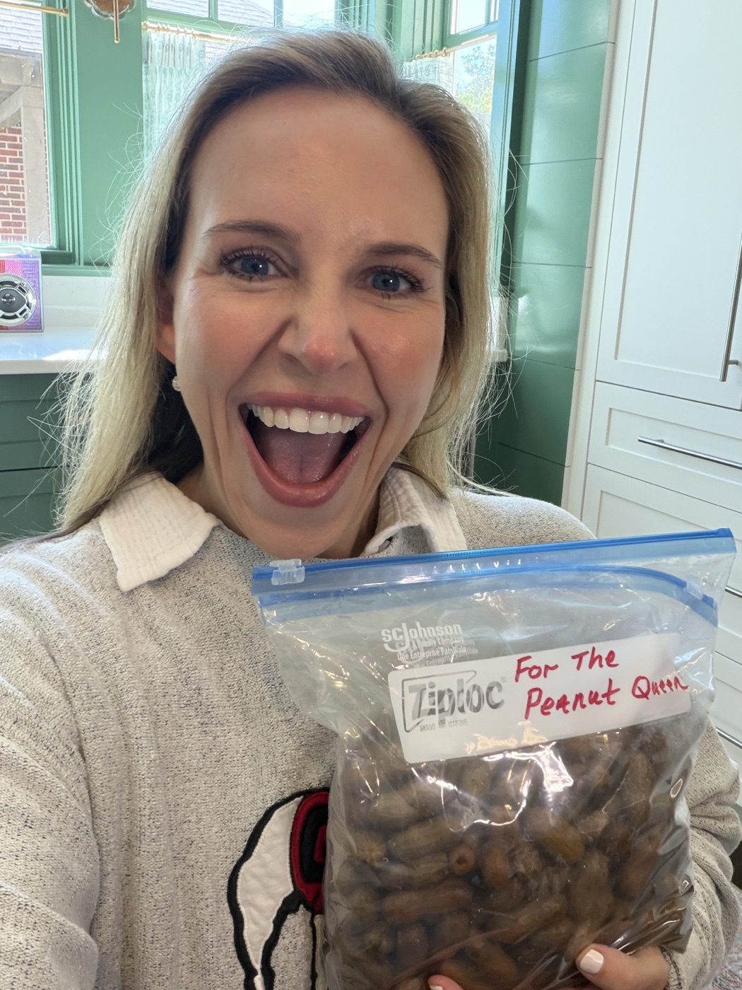 A smiling woman holding a bag of boiled peanuts labeled For The Peanut Queen